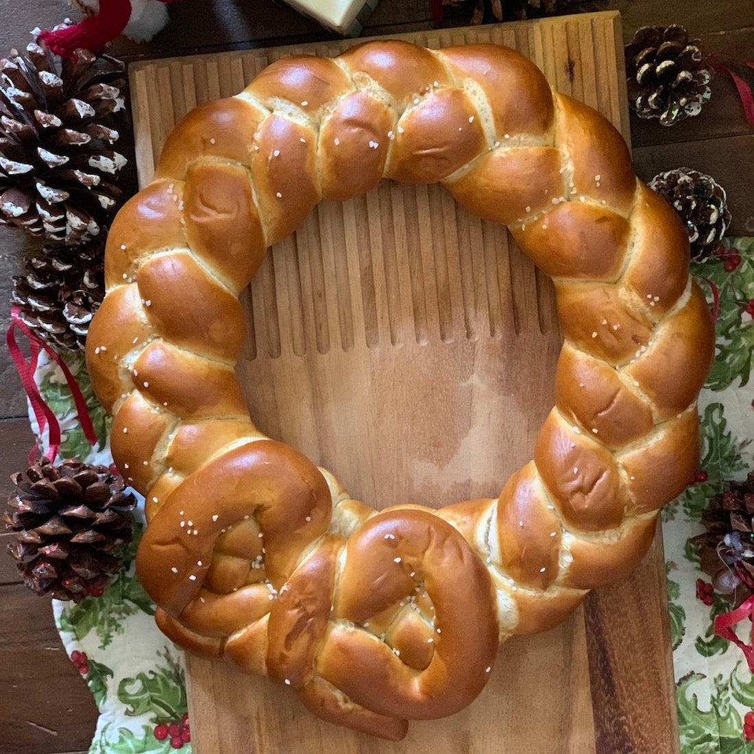 Large pretzel twist in the shape of a holiday wreath on a table next to pinecones and a holiday table cloth